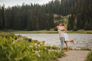 Couple strolling along a scenic mountain lake trail surrounded by pine trees and natural beauty.