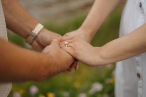 Close-up of hands holding and petting a small white dog during an outdoor photoshoot.