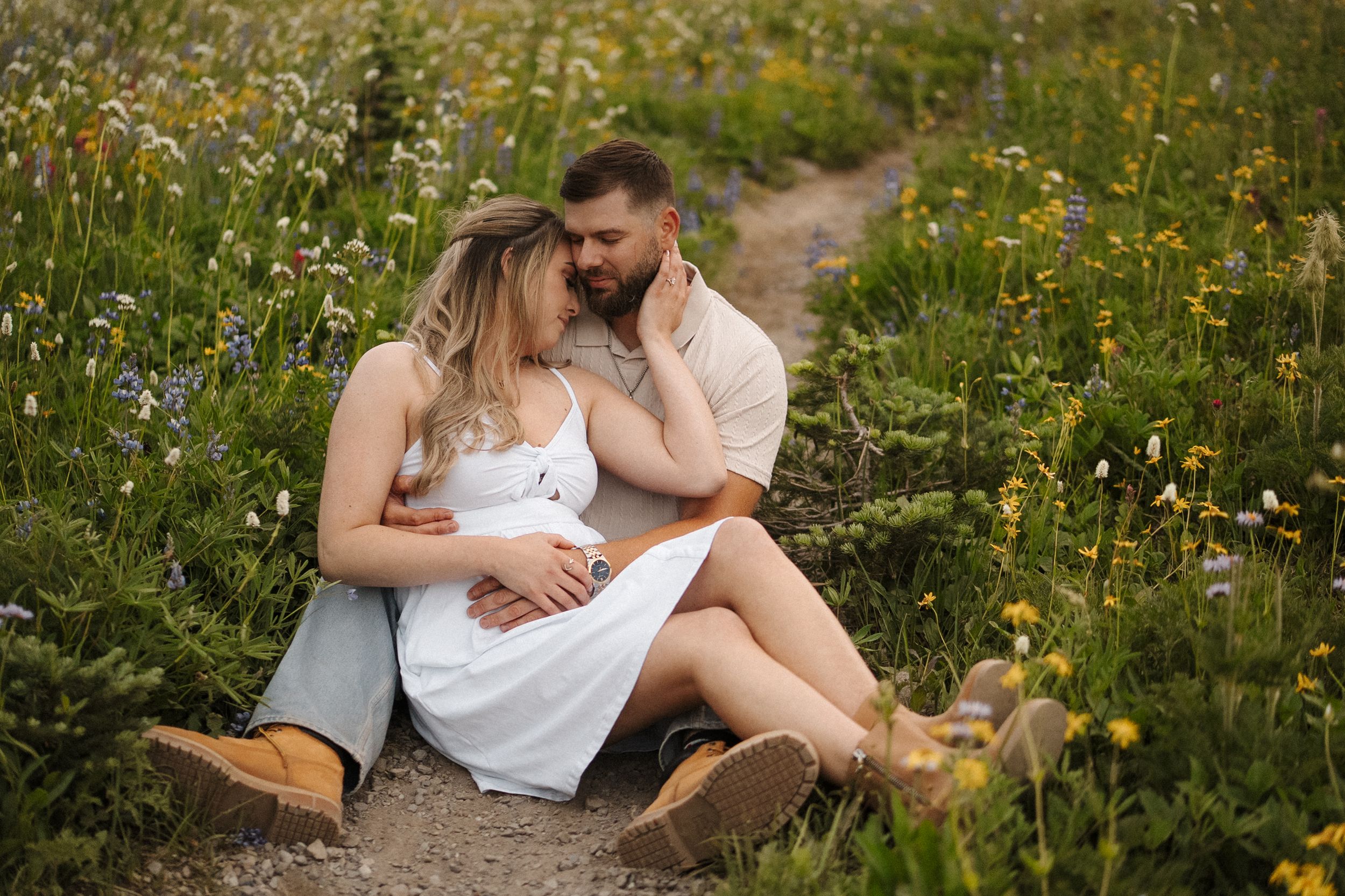 Couple embraces tenderly in a meadow of wildflowers during a sunny summer afternoon.