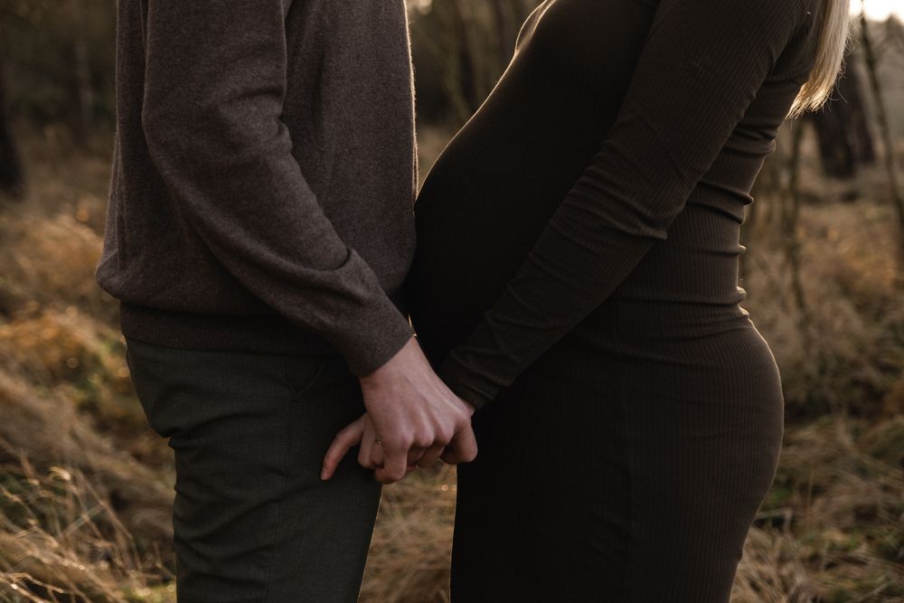 Close-up of two people holding hands in casual clothing standing in a field at sunset.