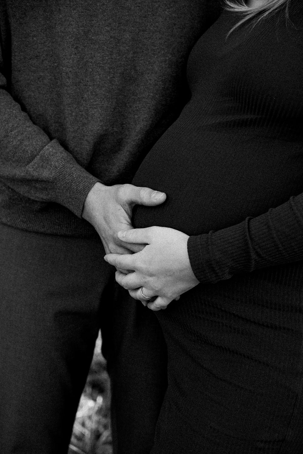 A black and white photo of hands tenderly cradling a pregnant belly, showing an intimate maternity moment.