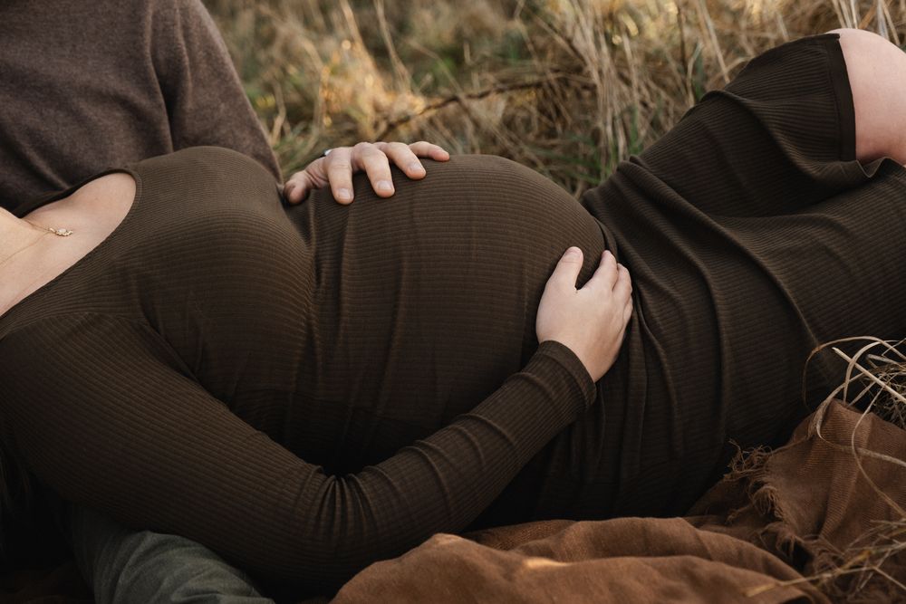 A couple in dark clothing lies close together on grass during an intimate outdoor photo session.