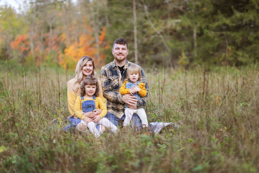 Family sitting together on a rustic wooden bench in a scenic autumn field during golden hour.