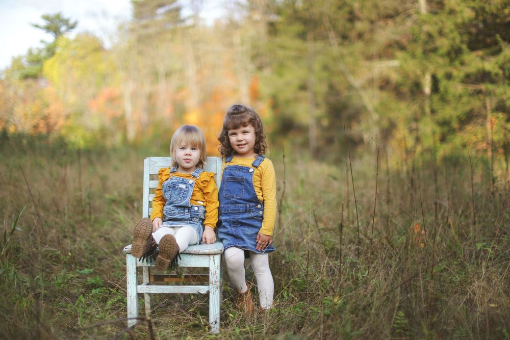 People gathered on a white wooden bench in a natural meadow setting with fall foliage in background.