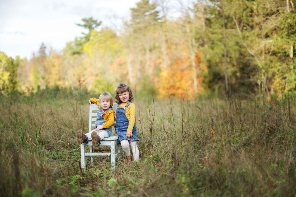 Family outdoor photo session in a field with autumn foliage and trees in the background.