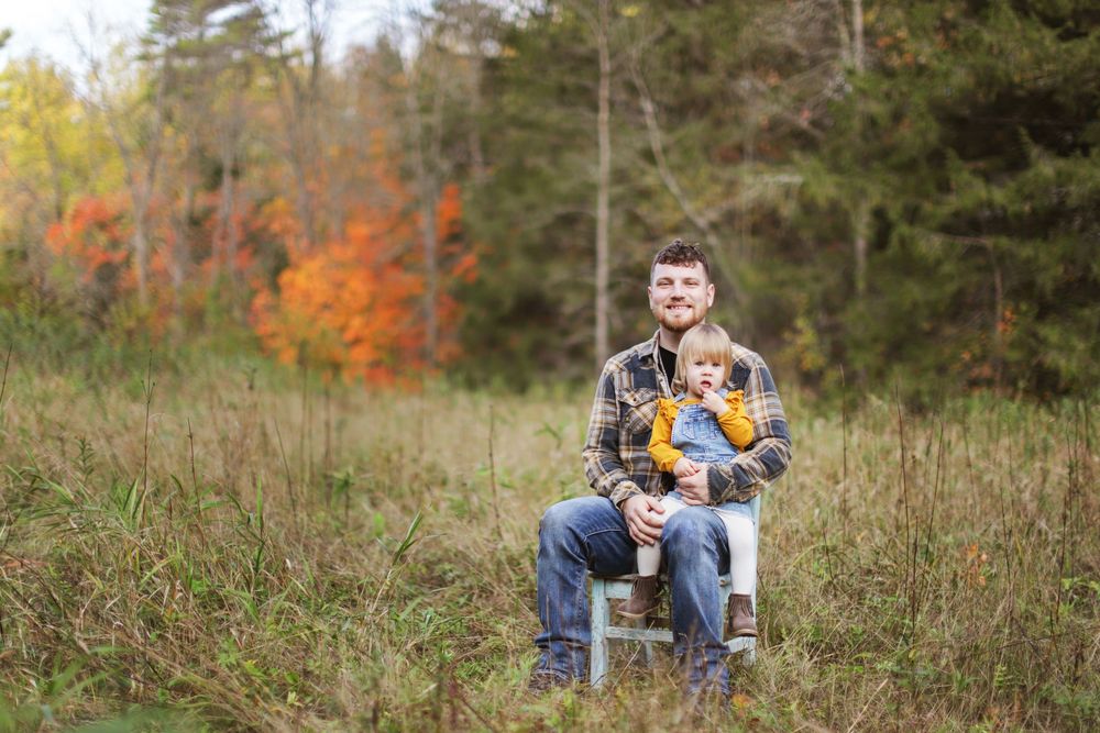 Family enjoying fall photo session outdoors with white chair in rustic field setting.