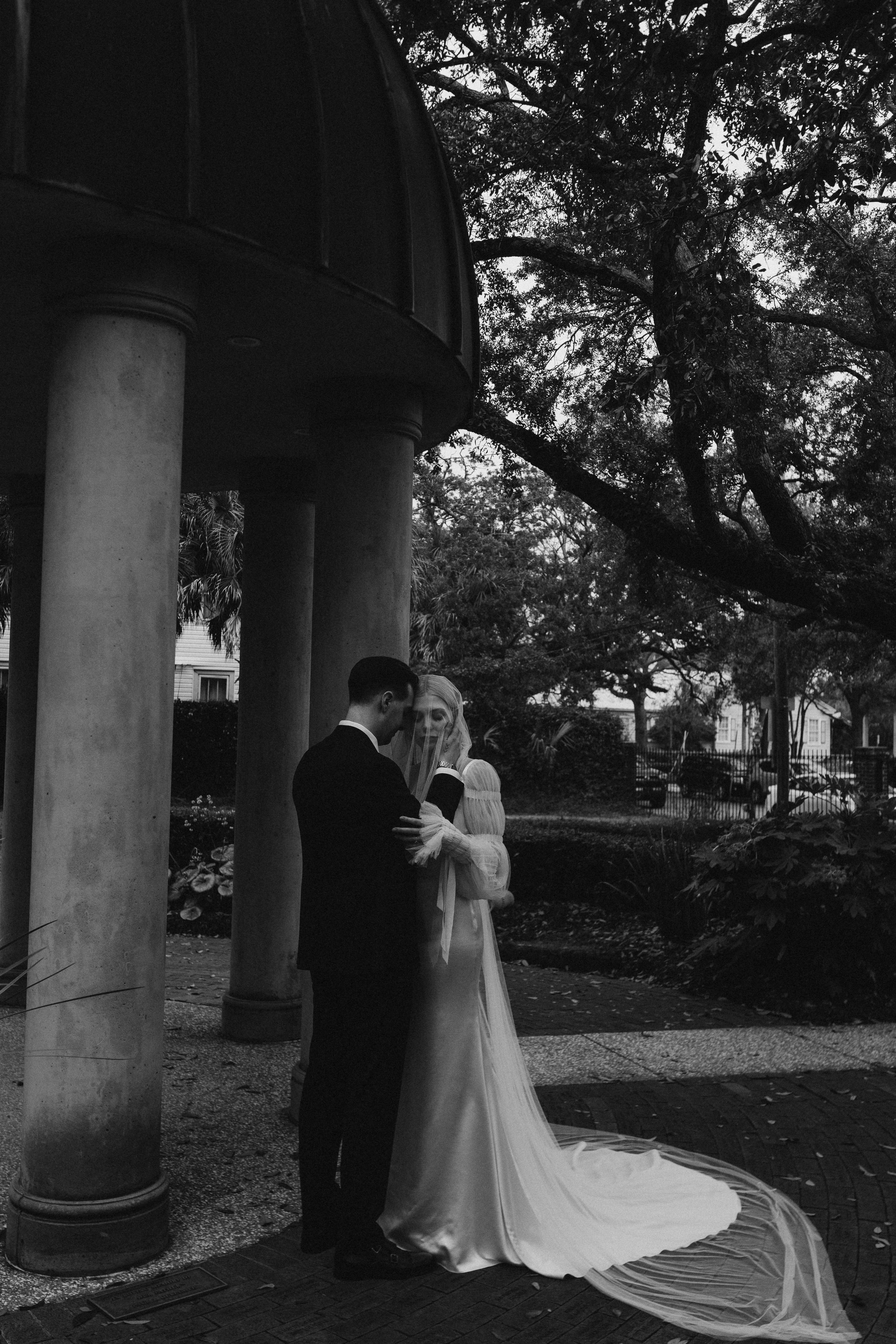 A black and white photo series showing a couple in wedding attire standing between outdoor stone columns.