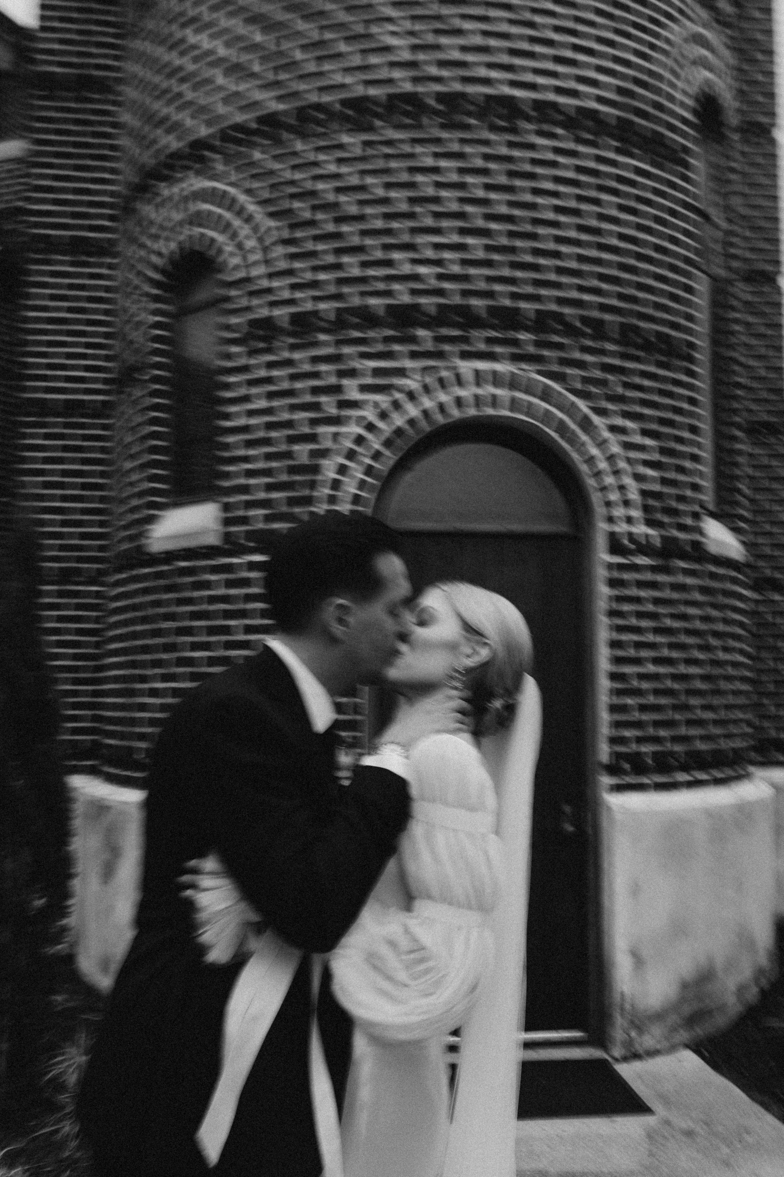 A romantic black and white sequence of a couple sharing a kiss against a brick wall exterior.