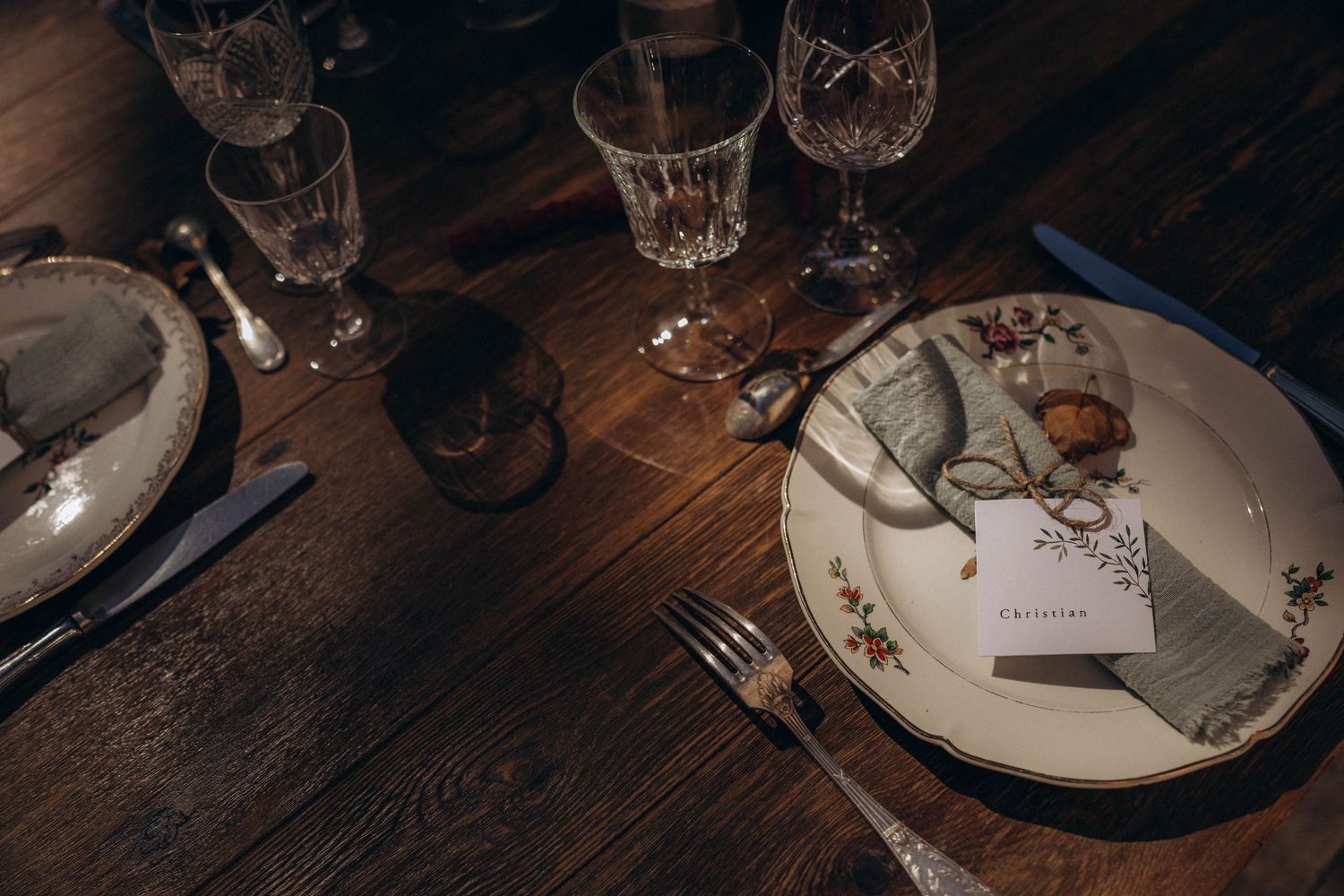 A rustic wooden table set for dinner with wine glasses and plates in a dimly lit restaurant setting.