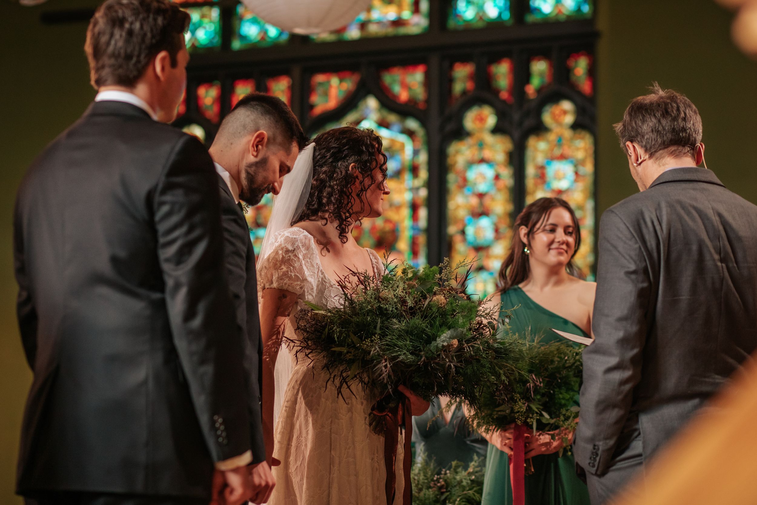 Wedding ceremony taking place in a church with stained glass windows and people gathered at the altar.