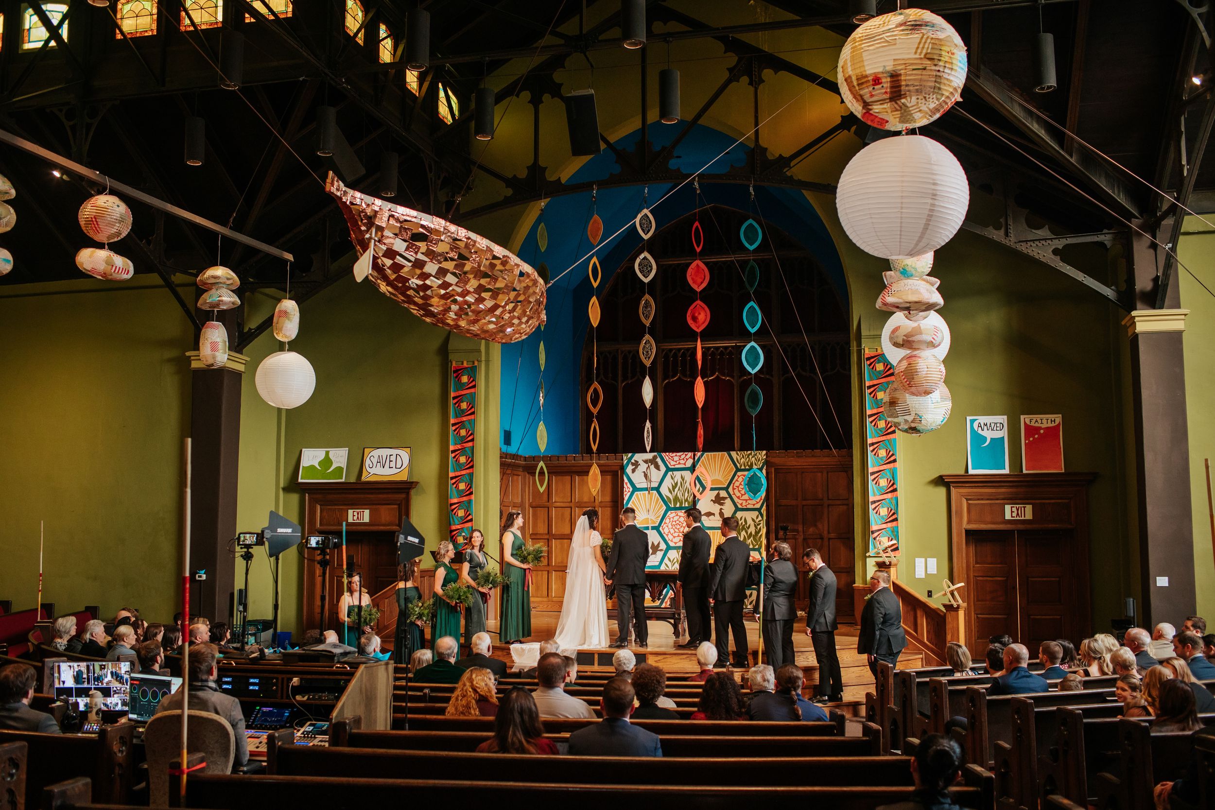 Interior view of a dimly lit church sanctuary with decorative hanging lights and wooden beams during a service.