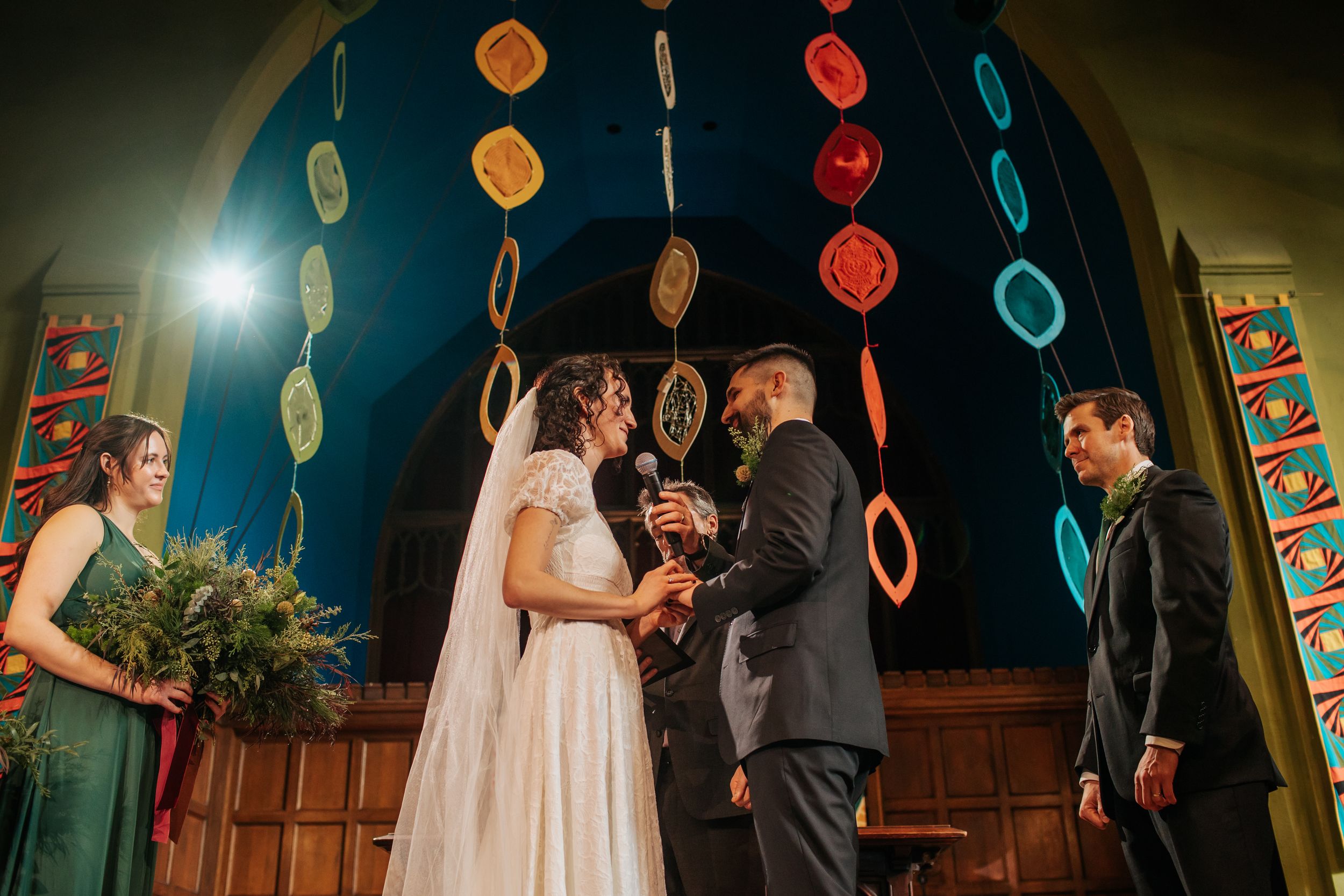 A wedding ceremony takes place under colorful hanging paper lanterns in a dimly lit wooden interior space.