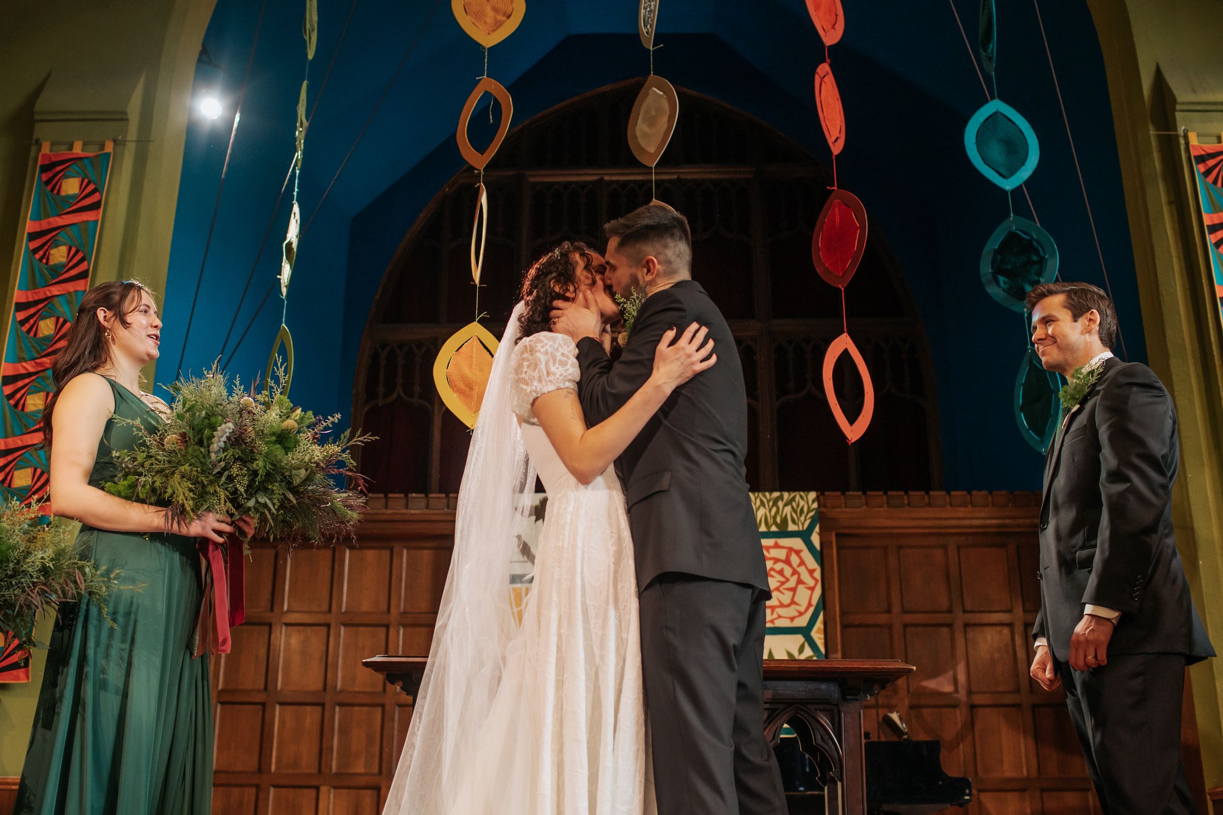 Joyful wedding party dancing and celebrating under colorful hanging decorations in a rustic wooden venue.