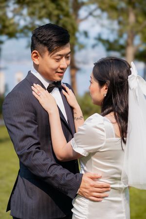 A romantic wedding couple embraces outdoors in a garden setting, with the bride in white and groom in pinstripe suit.
