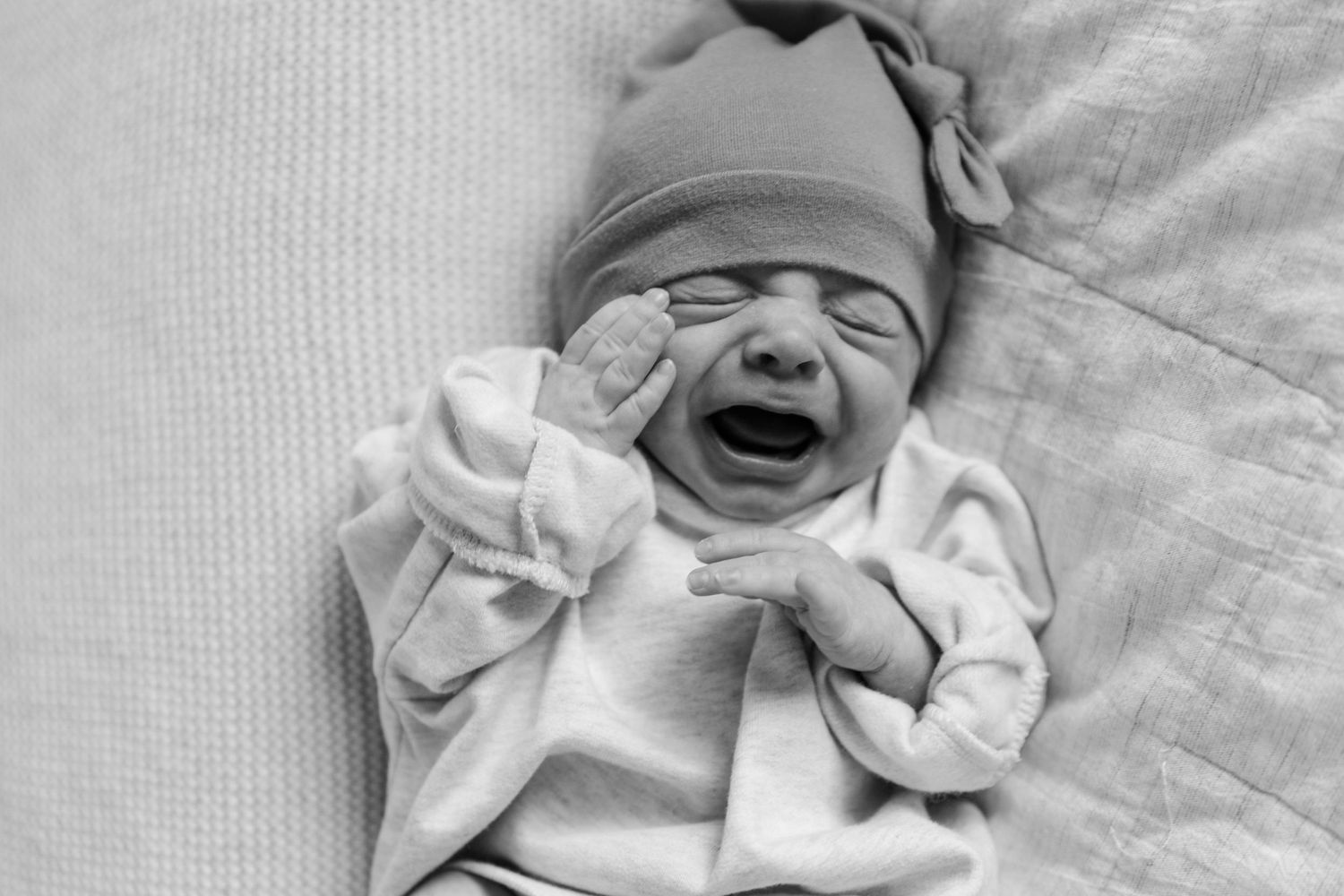 b&w newborn crying wearing a beanie and oversized shirt
laying on bed