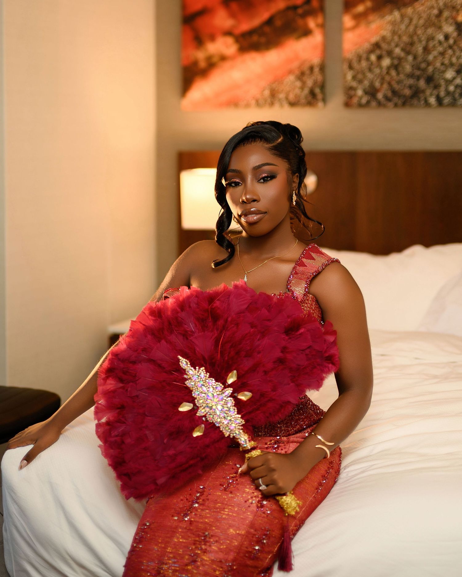 A glamorous boudoir photo session featuring a woman in a red feathered dress posing elegantly on a bed.