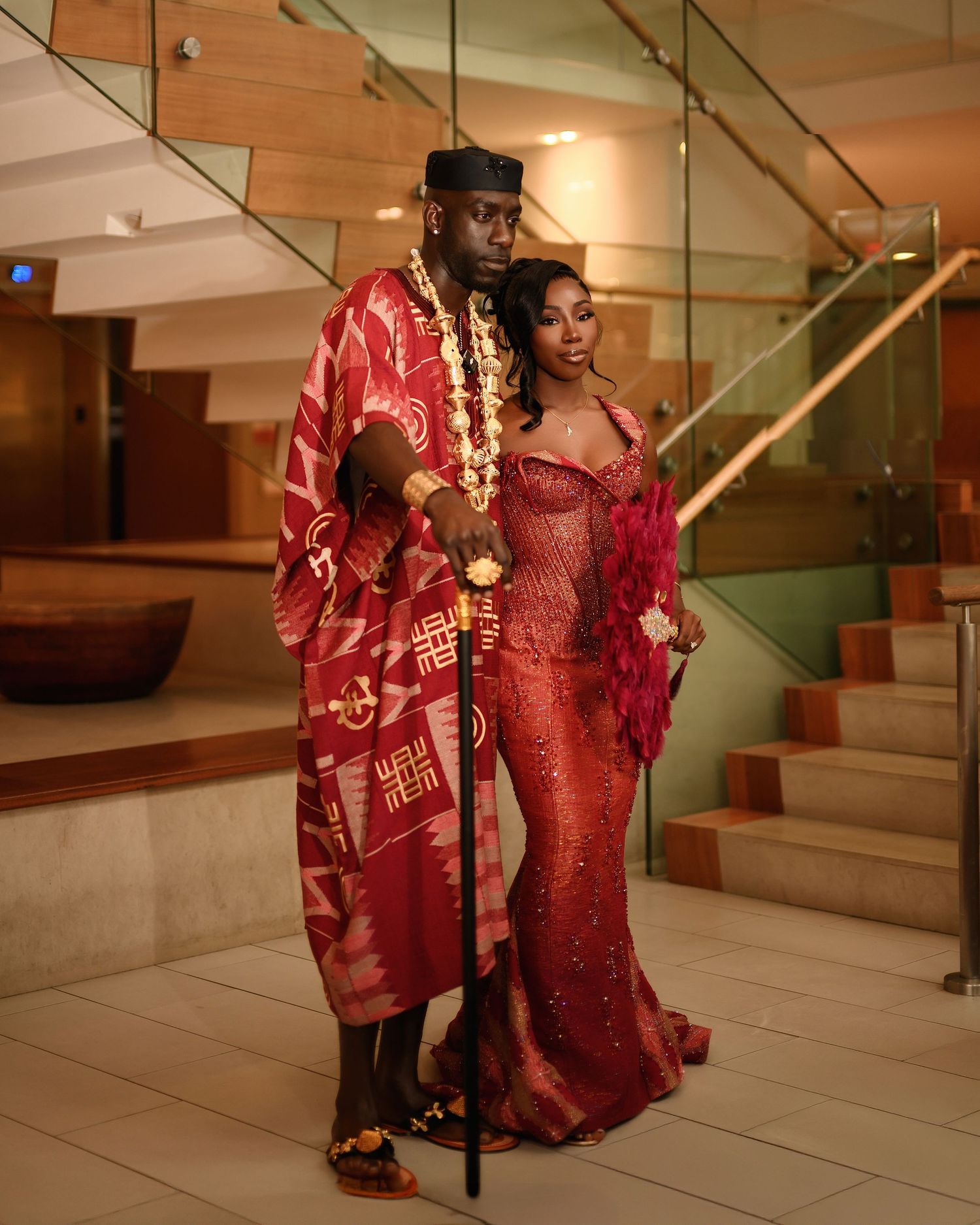 A figure in a shimmering red sequined gown and matching jacket poses dramatically on a modern staircase.