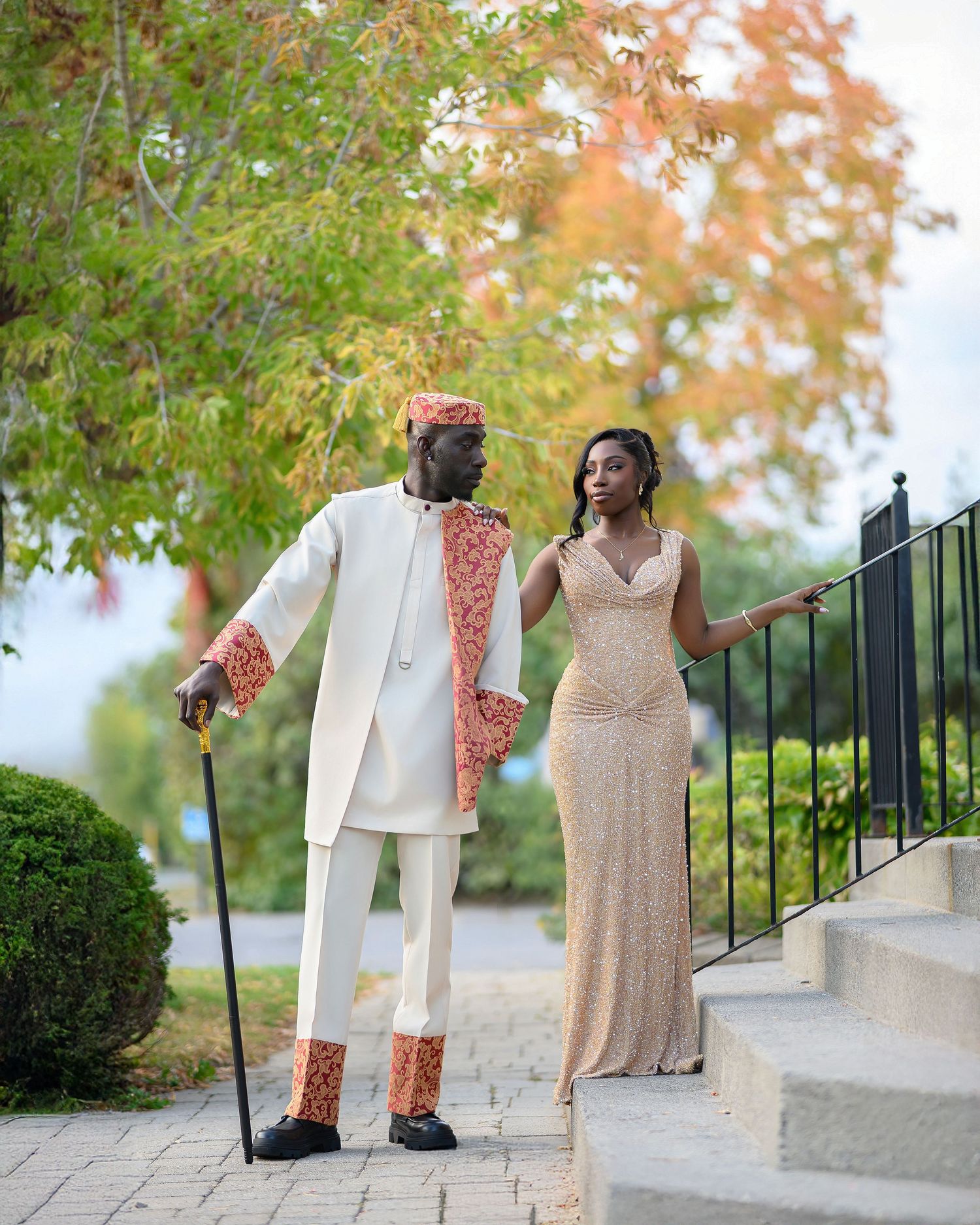 A couple in formal attire stands together on stone steps during an outdoor autumn photo session.