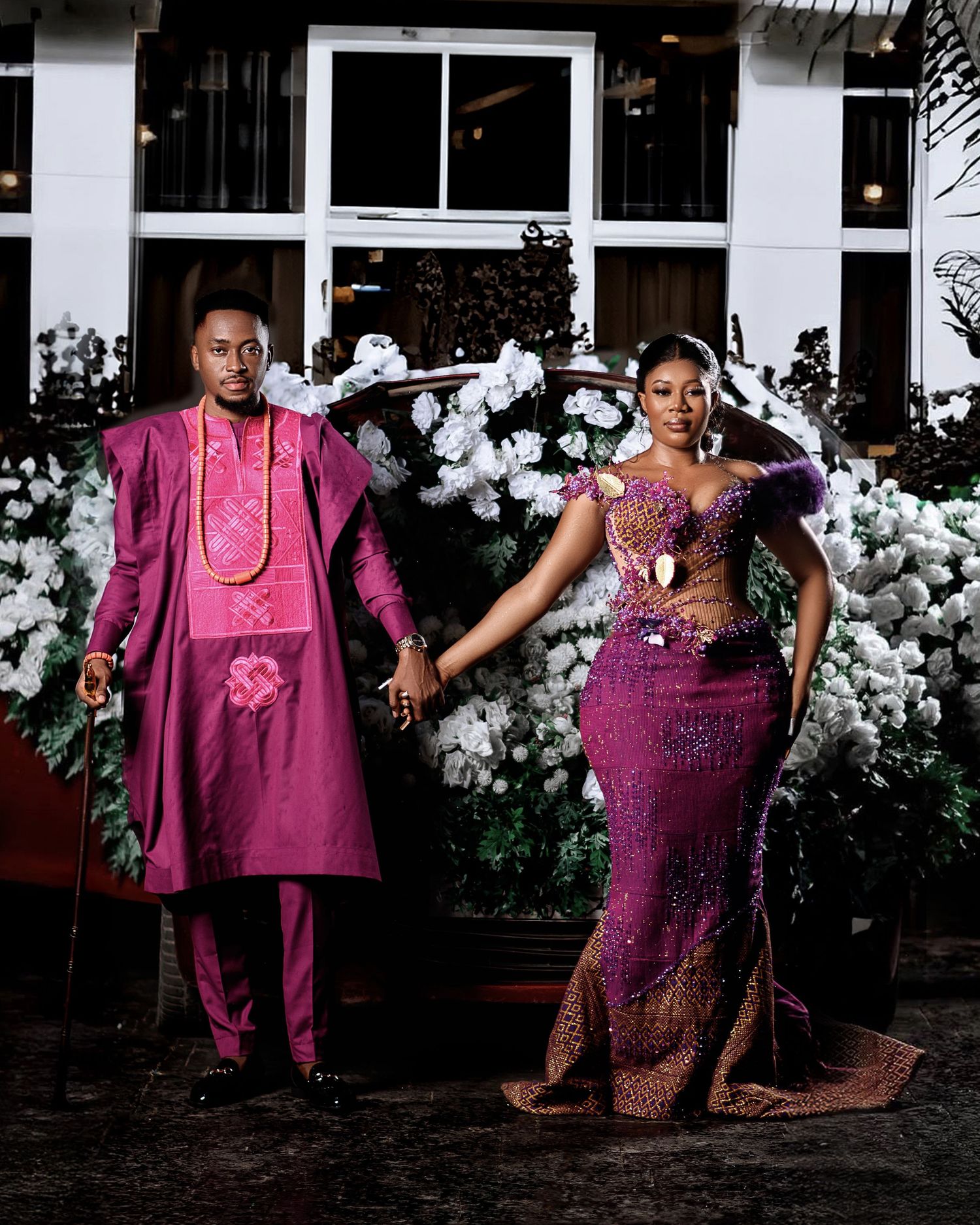A group of people wearing coordinated magenta and purple formal outfits pose together in front of a white building.