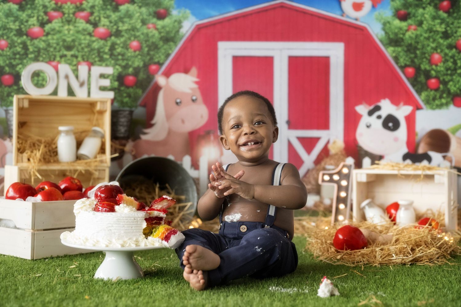 Farm-themed first birthday party setup with red barn backdrop, cake, and barnyard decorations.