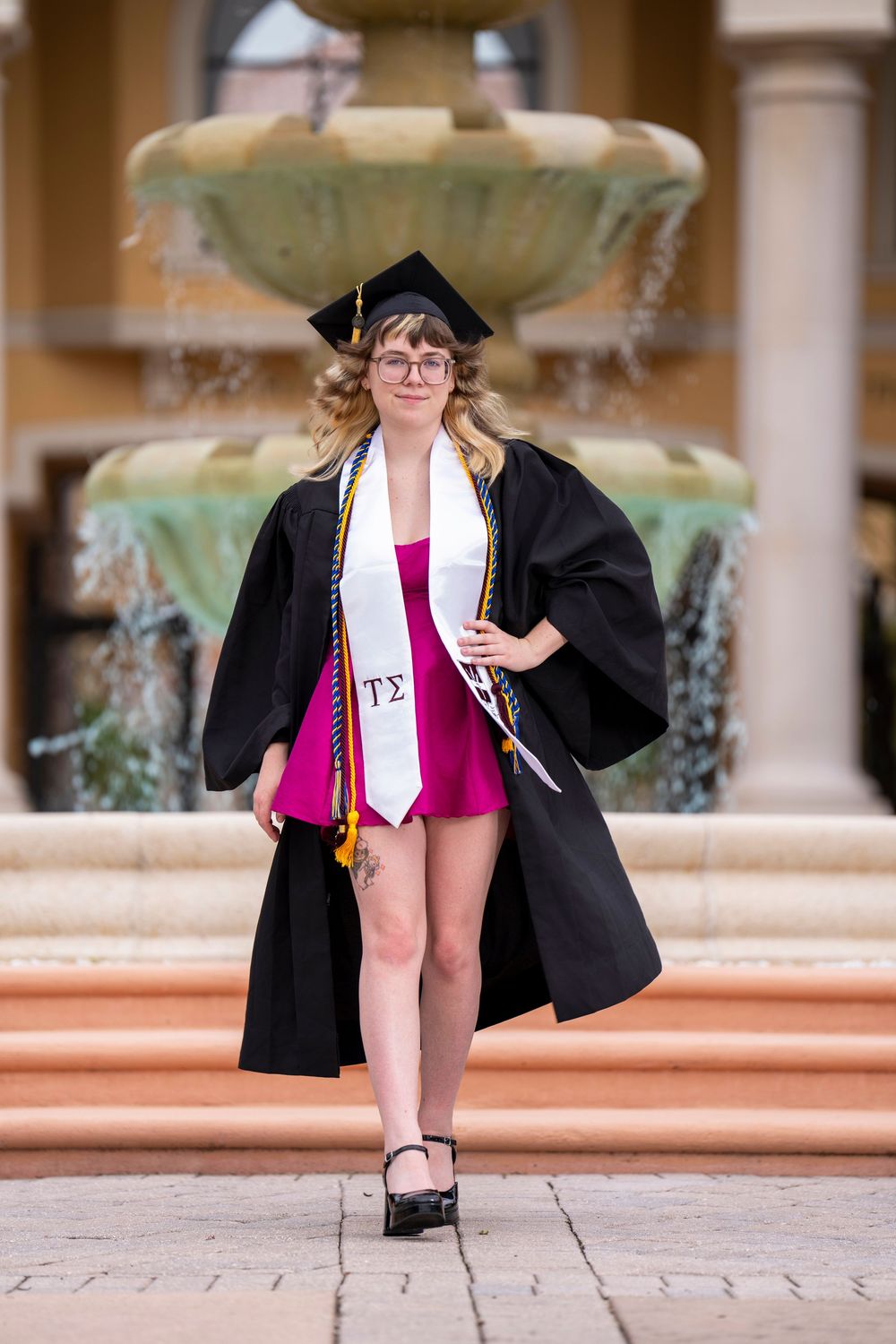 Graduate in black cap and gown with pink dress poses in sequence of celebratory graduation photos on campus steps.