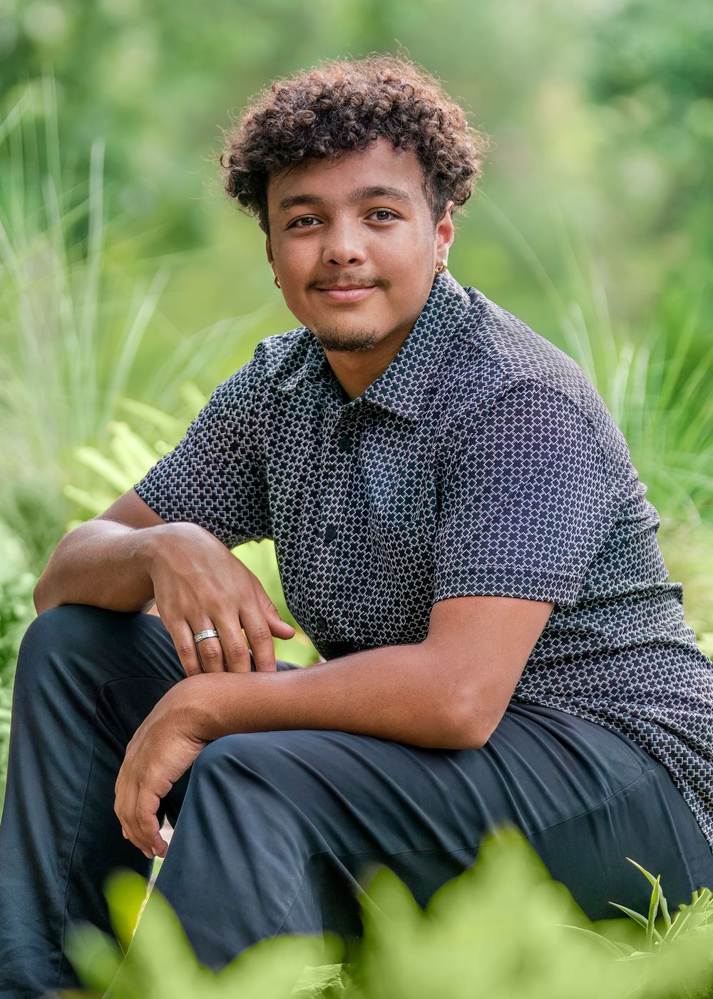 A person in a polka dot shirt sits casually in green grass during an outdoor photo session.