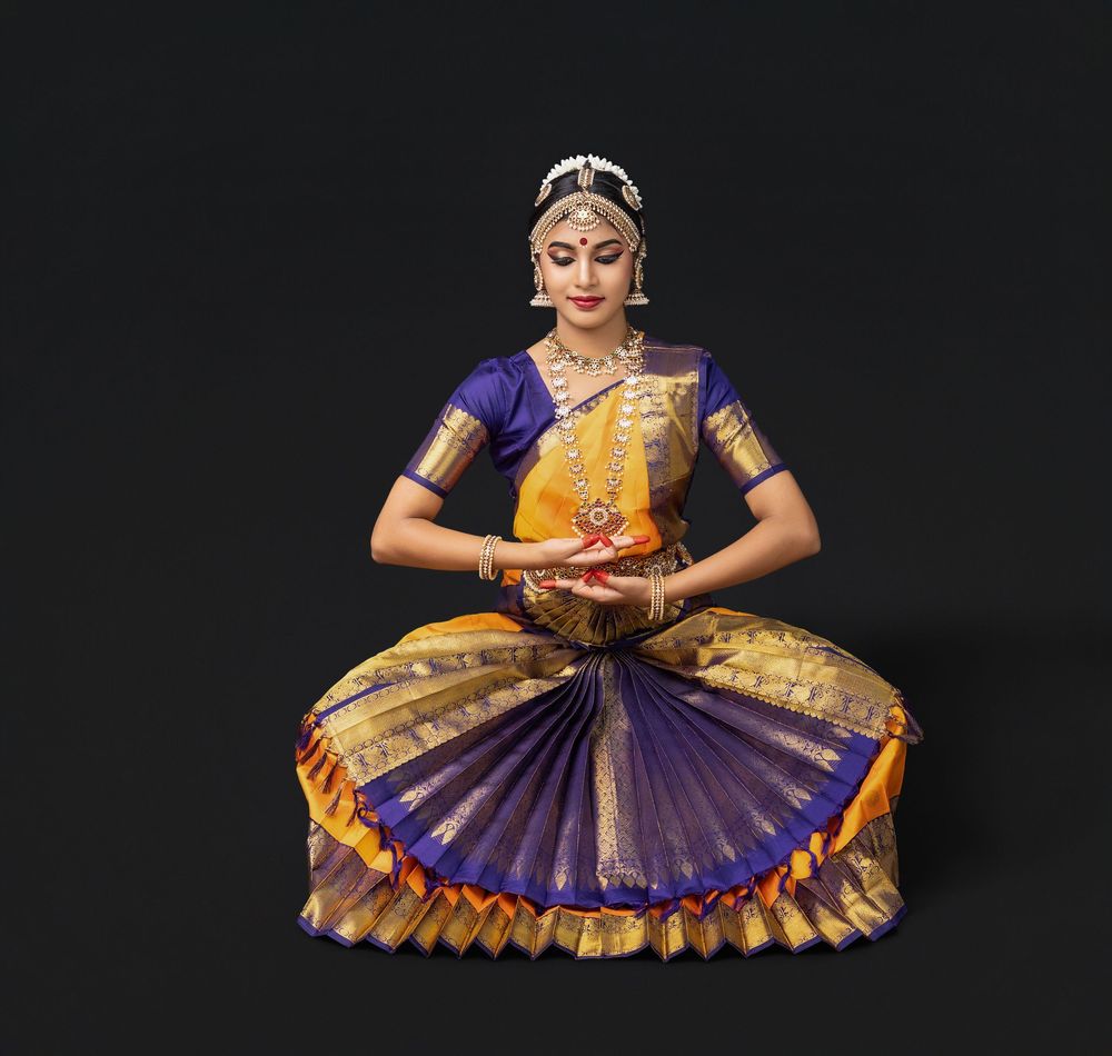 Classical Indian dancer in traditional yellow and purple costume performs elegant hand gestures and poses.