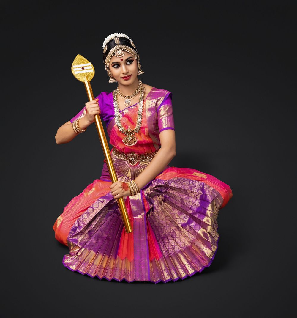Classical Indian dancer in vibrant pink and purple traditional costume performs graceful movements against dark background.