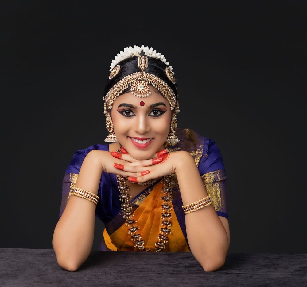 Traditional Indian dancer wearing ornate jewelry and colorful attire poses expressively against dark background.