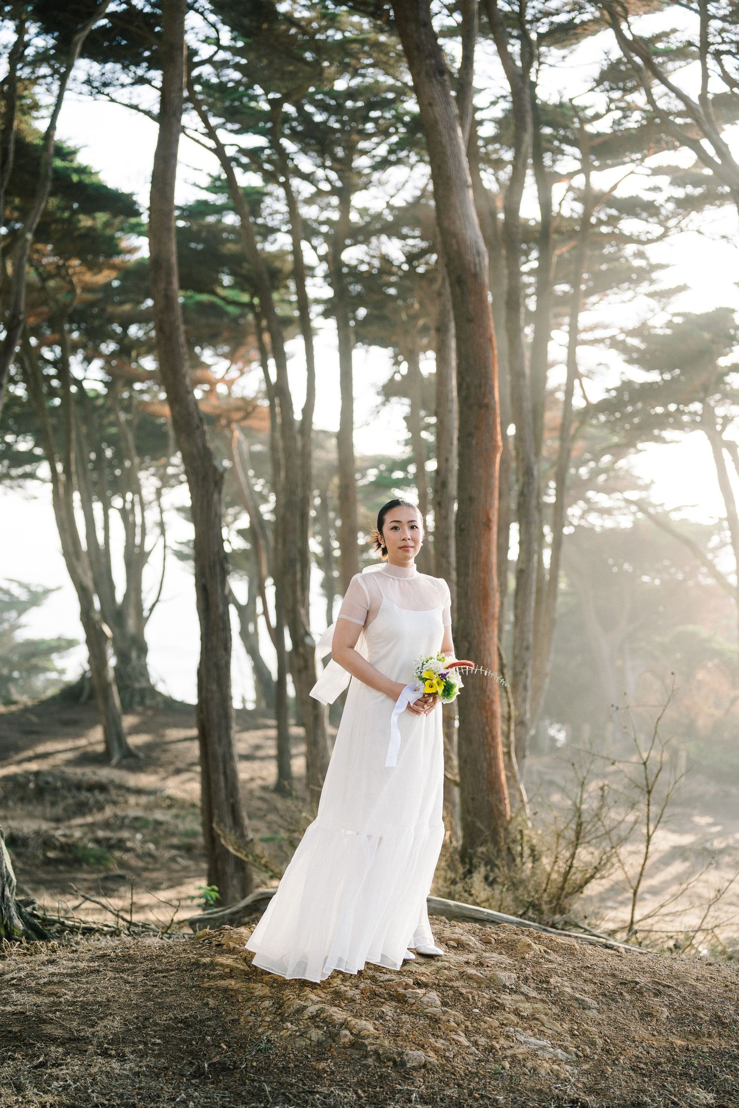 A scenic wedding photoshoot among tall pine trees at sunset with ethereal lighting and forest atmosphere.