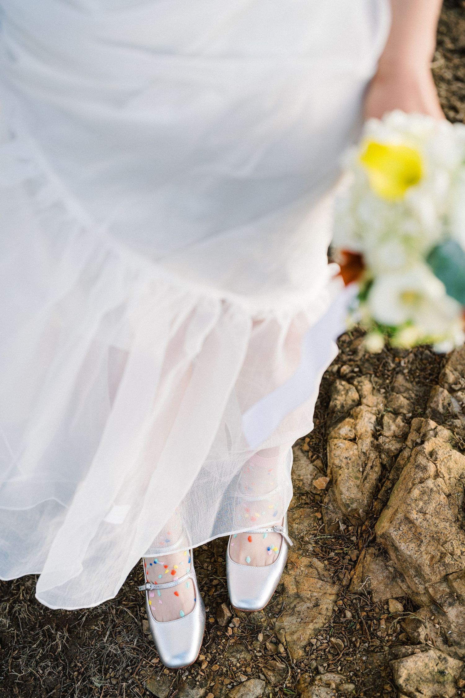 Close-up view of white wedding dress and shoes on rocky coastal terrain.