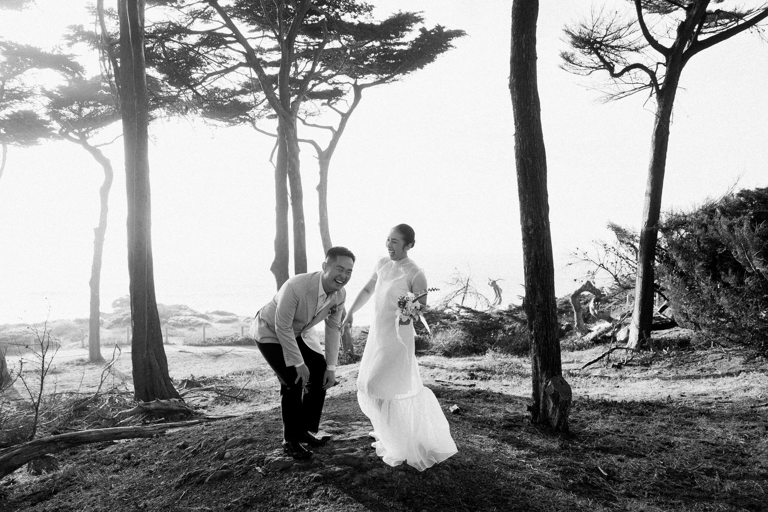 A romantic wedding couple walks through a misty forest setting captured in black and white photography.