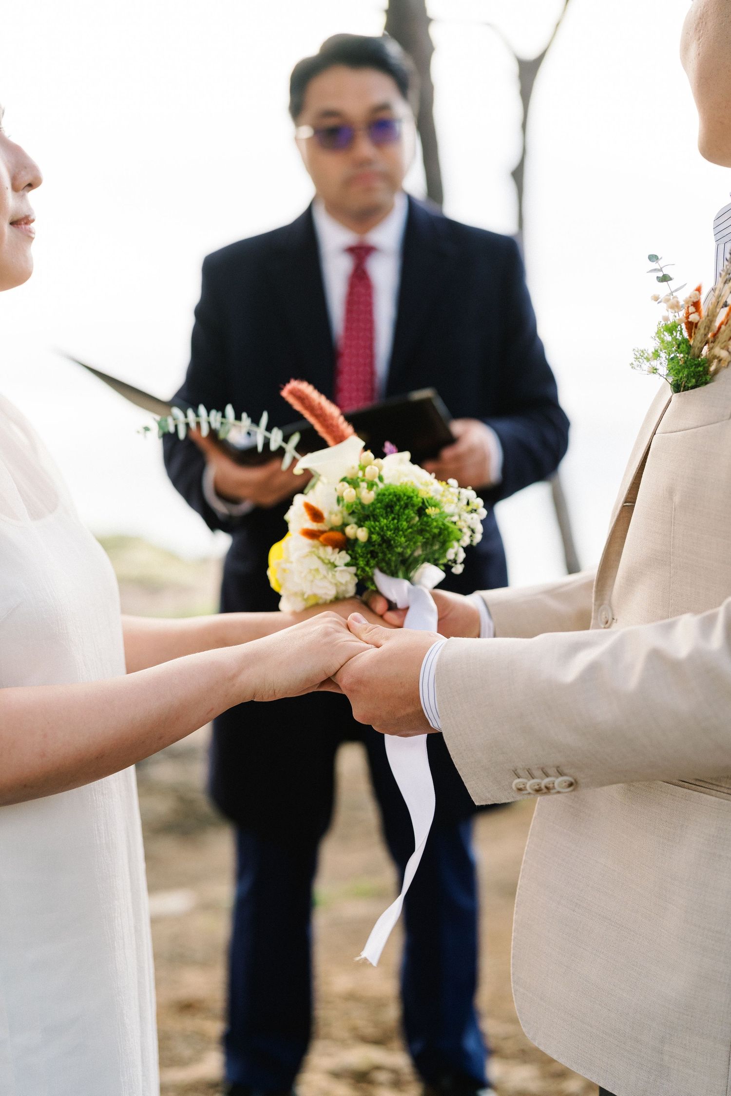 Wedding ceremony detail shots showing hands exchanging bouquets with white and yellow flowers.