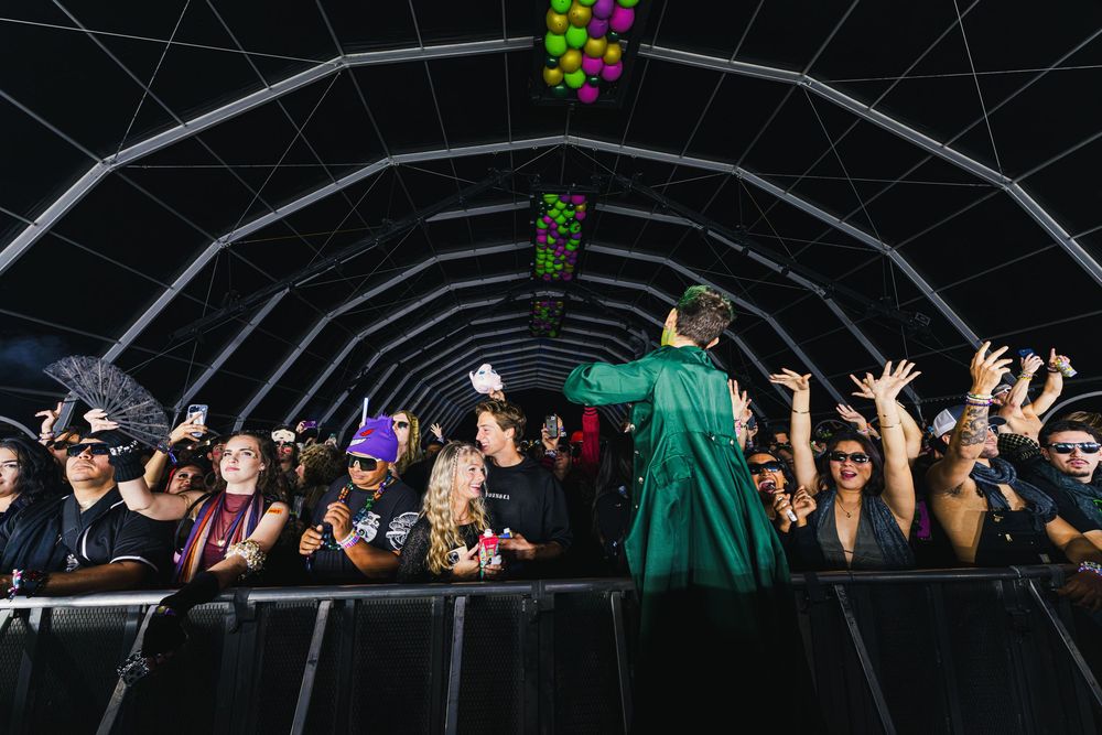 Energetic crowd at a music festival tent with colorful decorations and raised hands during a performance.
