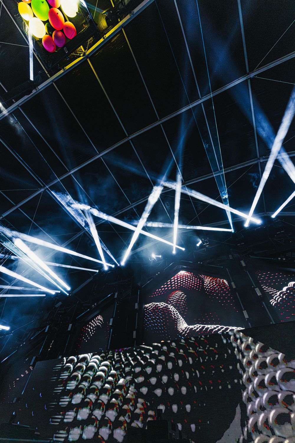 Concert venue with rows of empty seats illuminated by dramatic blue and white stage lighting from above.