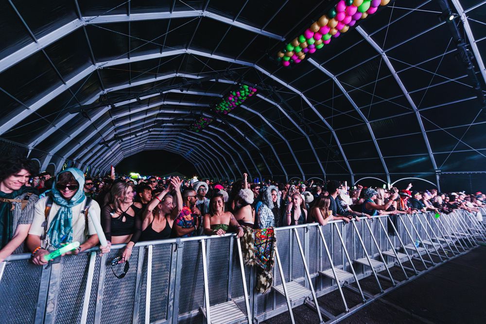Crowd of concert attendees walks through a dark tunnel illuminated by neon lights during a nighttime event.