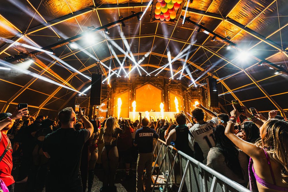 Concert crowd with raised hands enjoying a live performance under warm lighting in an indoor venue.