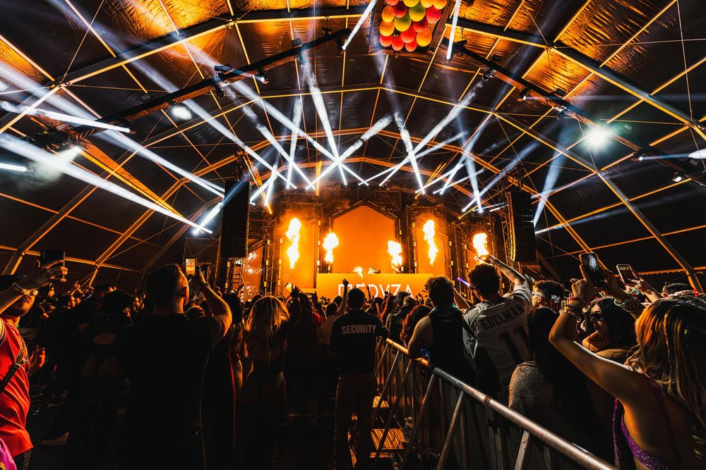 A large crowd gathers under a glowing canopy of lights at an evening event venue.