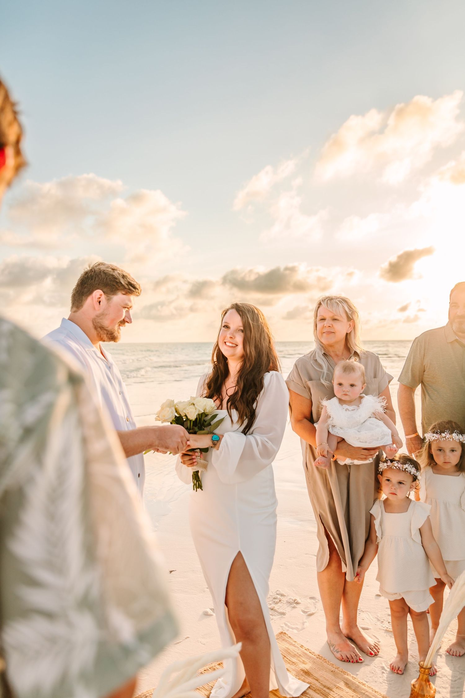 Family gathering on a sunny beach at sunset with warm golden light illuminating their casual white attire.