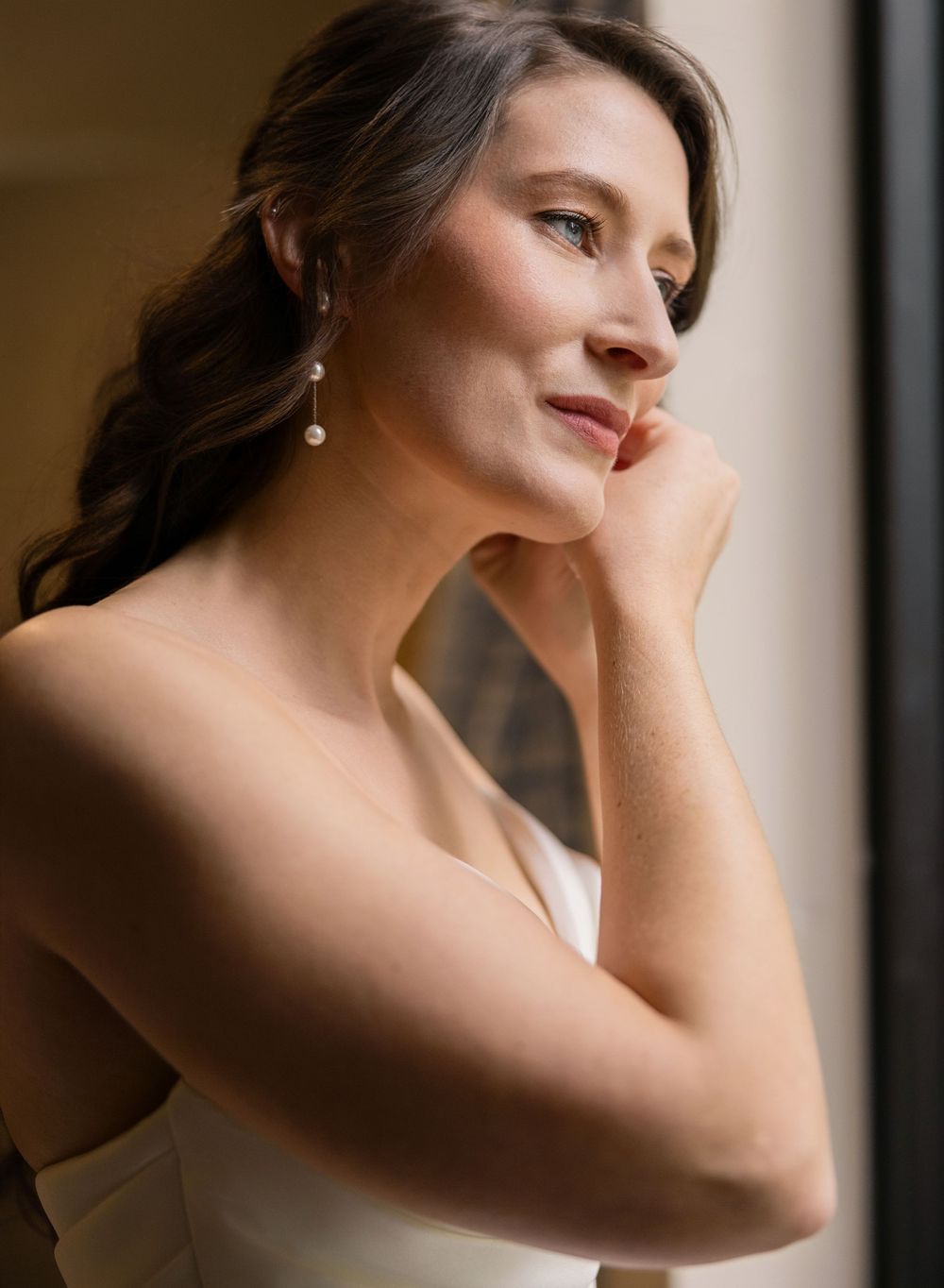 A woman in a white dress poses elegantly by a window in a series of soft, romantic bridal portraits. Columbus ohio.
