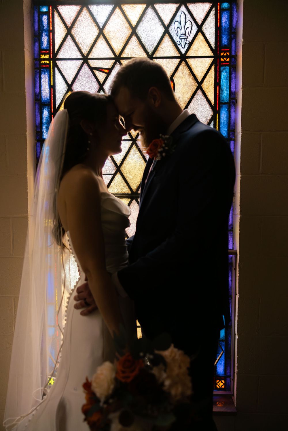 Silhouetted couple shares romantic kiss in front of stained glass church windows with beautiful lighting. Columbus Wedding
