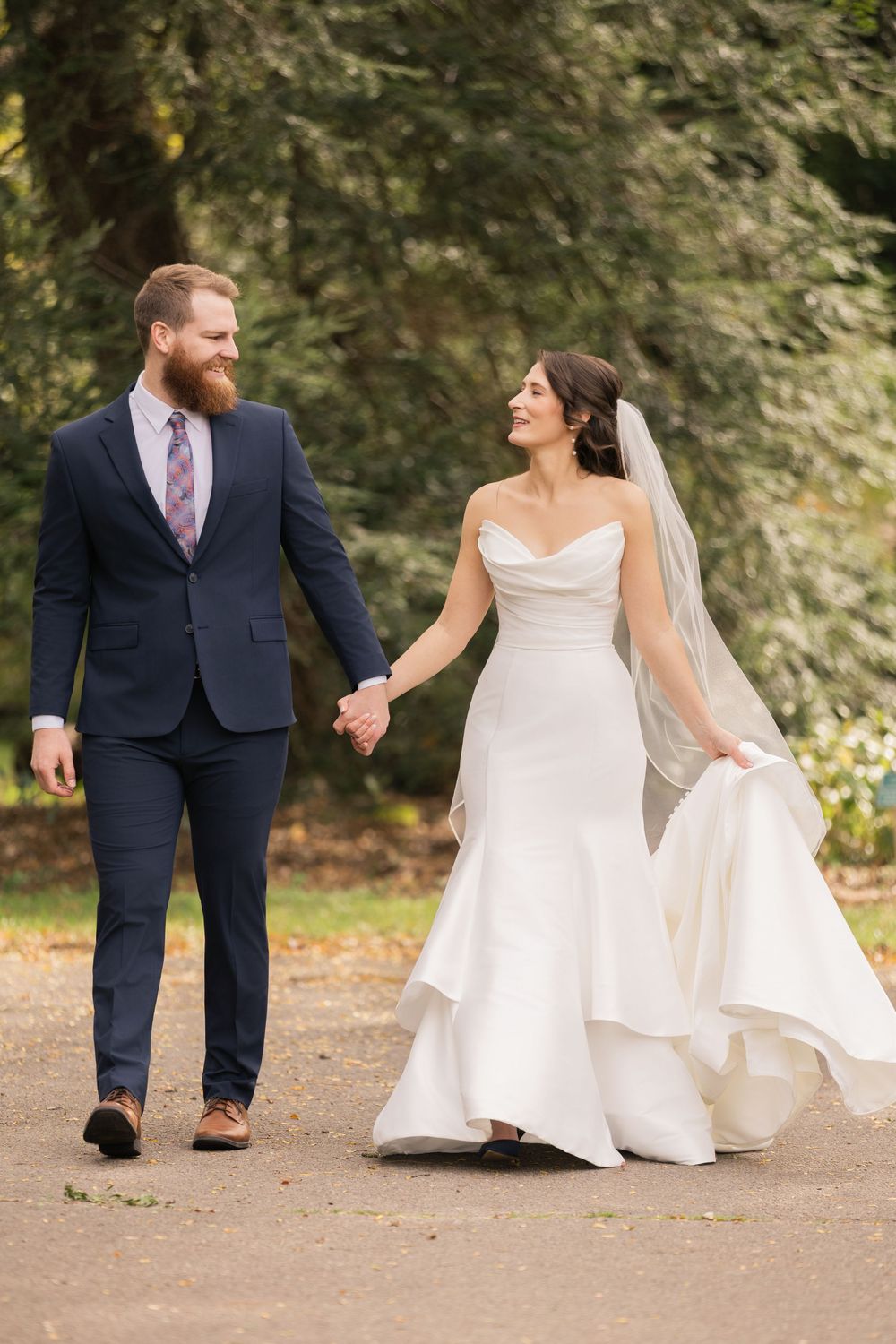 Romantic wedding couple poses playfully on autumn path in navy suit and flowing white gown. park of roses columbus ohio.