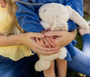 Adults and child holding a white stuffed bunny rabbit toy together outdoors. family session details, childs hands with mom. kimbell art