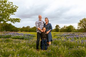 Family of three posing in a field of bluebonnets under cloudy skies in Texas. family session irving texas bluebonnets