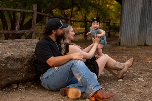 A couple sits together on a rustic wooden fence at sunset while another person sits in the background. Family session eagle mountain park
