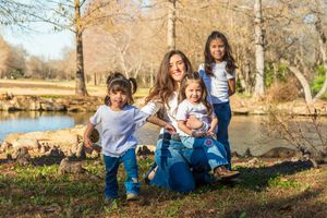 A family sits together outdoors on fallen autumn leaves during a sunny day in the park. fort worth botanic gardens family session