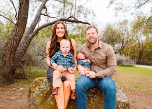 A group of people sit together on rustic wooden steps in a natural outdoor setting during autumn. Fort Worth Stockyards family session