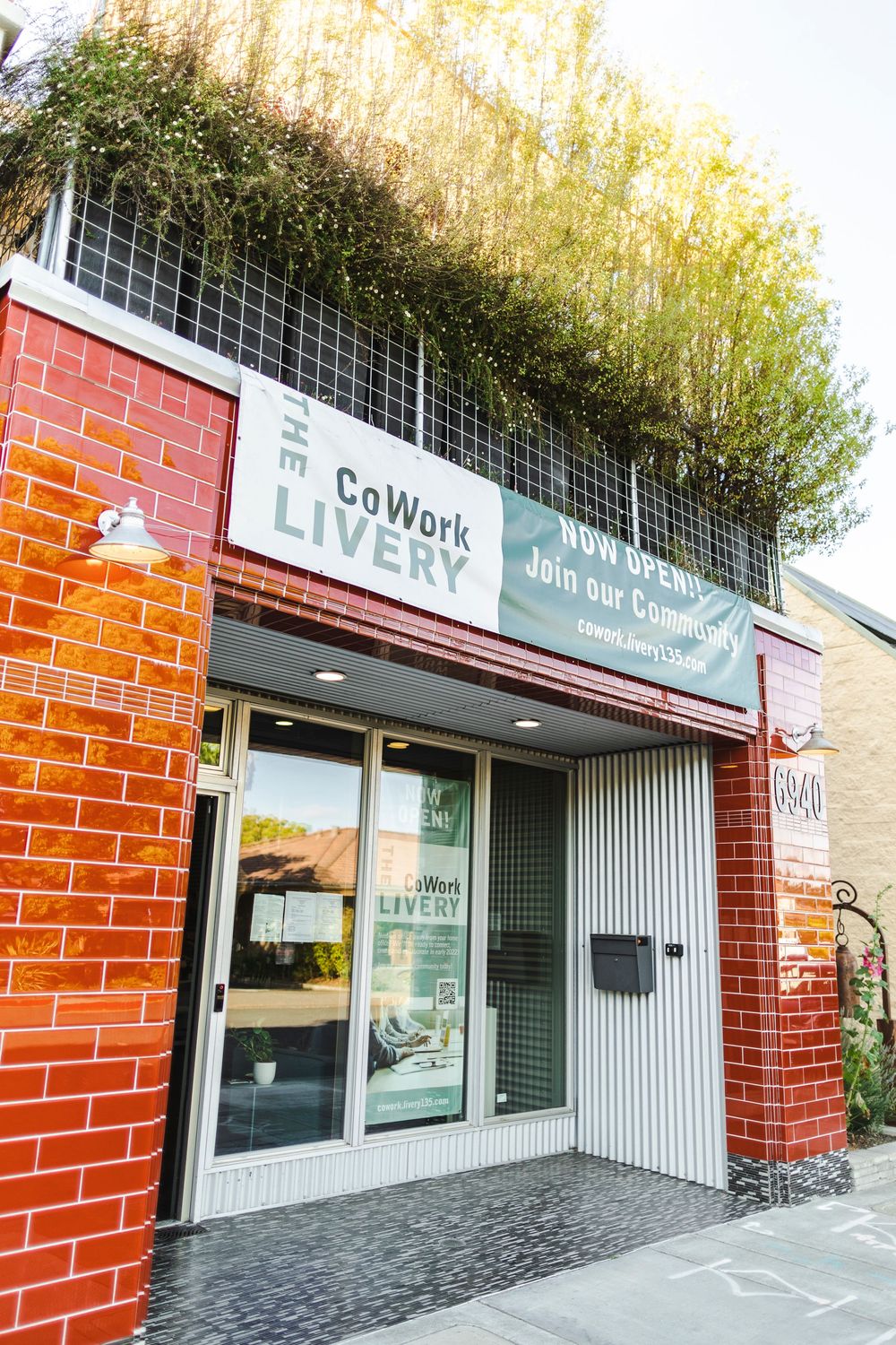 Modern coworking space entrance with red brick exterior and white signage for 'CoWork Live' in an urban setting.