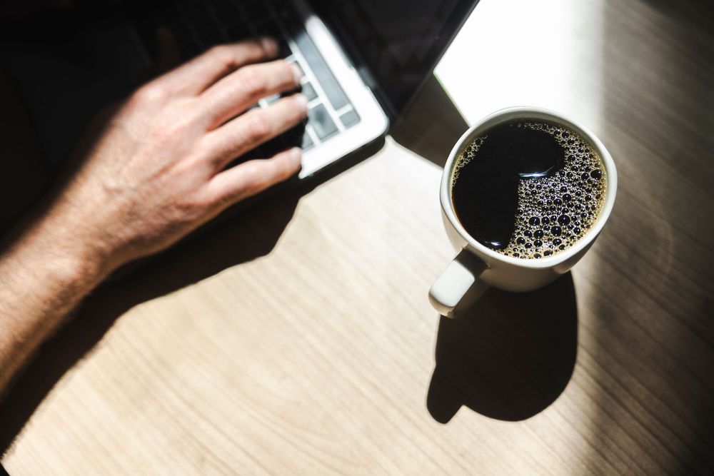 Coffee being poured into dark mugs on wooden table with dramatic lighting and shadows.