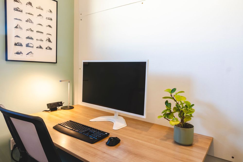 Modern home office setup with wooden desk, wall art, and minimalist decor in natural light.